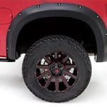Close-up of rugged off-road tires and black alloy wheels on a red pickup truck.