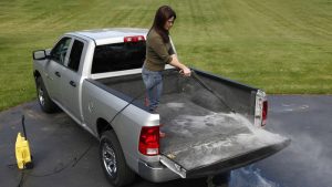 Woman cleaning a silver pickup truck bed with a power washer at Camp & Cruise.