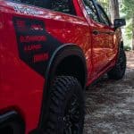 Close-up of a red off-road truck showcasing rugged tires, decals, and outdoor adventure features.