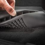 Close-up of car interior cleaning with a hand lifting a floor mat for detailed vacuuming.