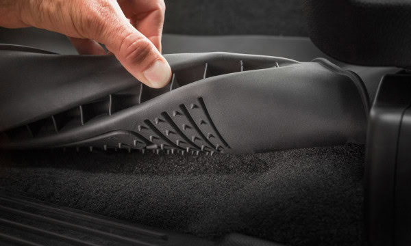 Close-up of car interior cleaning with a hand lifting a floor mat for detailed vacuuming.