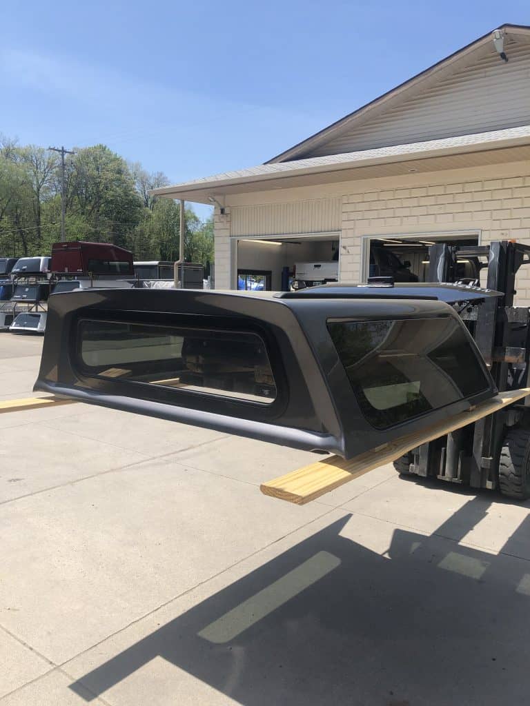 High-quality black truck cap being lifted for installation, ideal for pickup trucks at Camp & Cruise.