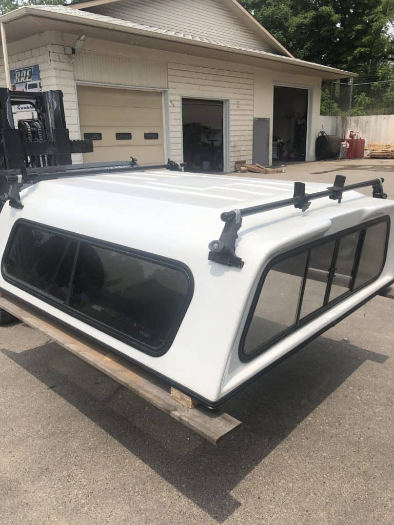 Durable white truck camper shell with tinted windows and roof rack system, ideal for outdoor activities.