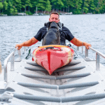 Man with kayak on lake at Camp & Cruise boat rental facility.
