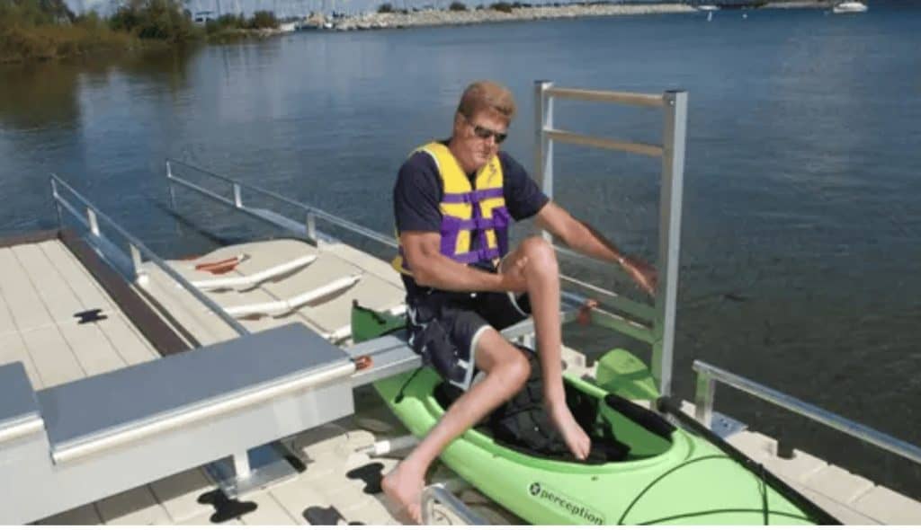 Person entering a bright green kayak at a lakeside docking station with safety gear.