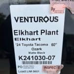 Inspection tag on Toyota Tacoma truck with details and barcode.
