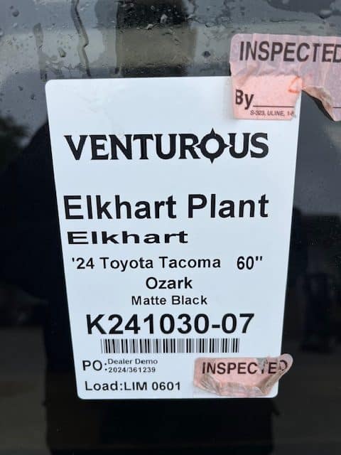 Inspection tag on Toyota Tacoma truck with details and barcode.