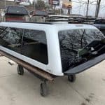 Silver truck cap for Nissan Titan with tinted windows and roof rack.