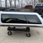 Silver truck cap with tinted windows for Nissan Titan on a cart.