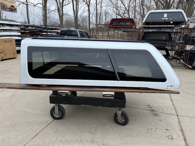 Silver truck cap with tinted windows for Nissan Titan on a cart.