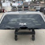Gray truck bed cap for GMC 1500 with window and mounting hardware.