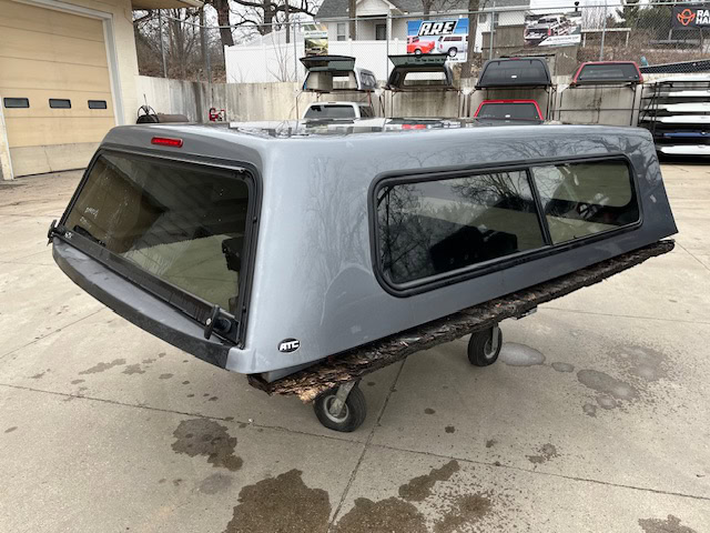 Gray truck cap with windows for Chevy 1500 8' bed, outdoor setting.