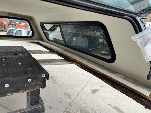 Side window of a truck cap with tinted glass and black frame.