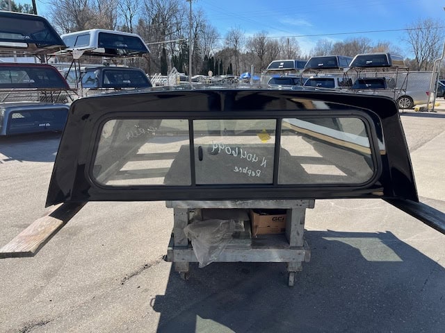 Black truck cap window for Chevy 1500 with tinted glass and aerodynamic design.