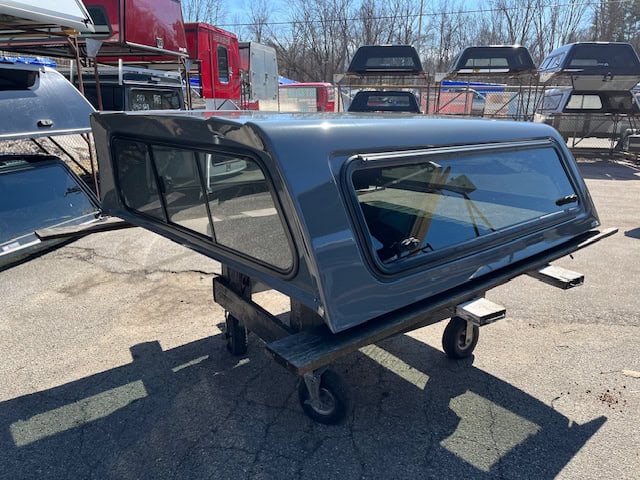 Black truck cap with tinted windows for RAM 1500, on a wheeled stand.