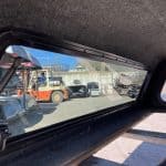 View through truck bed cover showing yard with equipment and vehicles.