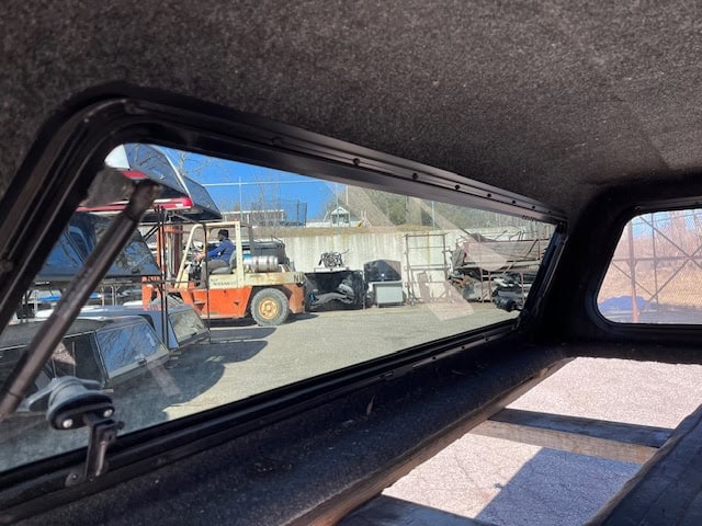 View through truck bed cover showing yard with equipment and vehicles.