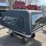 Gray truck bed cap for GMC 1500 with windows and mounting hardware.