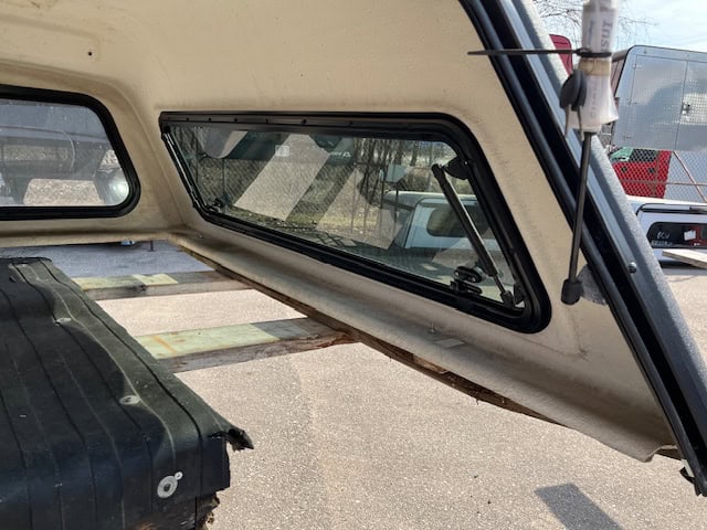Side window of GMC 1500 truck cap with tinted glass and black frame.