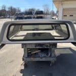 Silver truck bed cap for Ford F150 with tinted rear window.