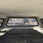 View of truck bed cover inside a Ford F150 with rear window and parked vehicles.