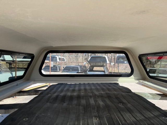 View of truck bed cover inside a Ford F150 with rear window and parked vehicles.