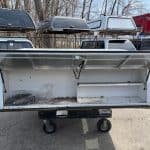 White truck bed storage box with open lid and wheels for easy transport.