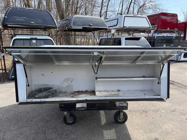 White truck bed storage box with open lid and wheels for easy transport.