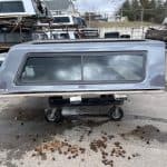 Gray truck camper shell with window for Ford F150 in storage lot.