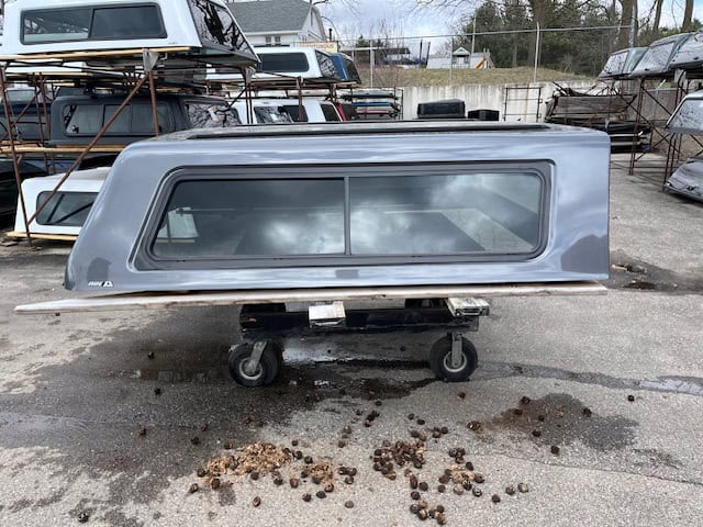 Gray truck camper shell with window for Ford F150 in storage lot.