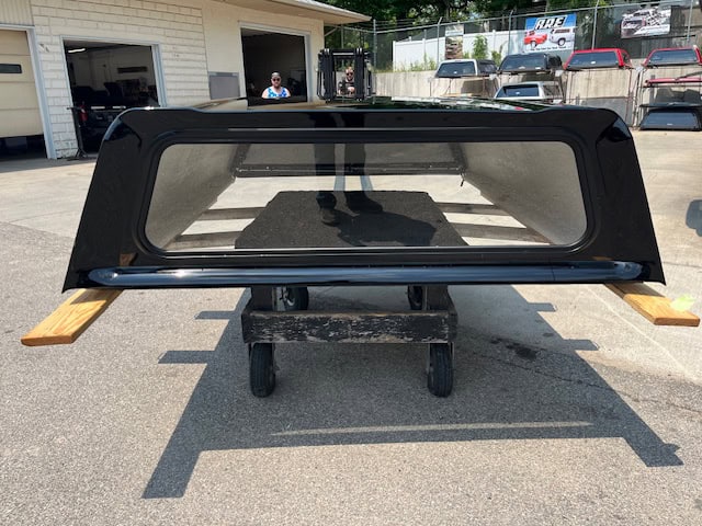Black truck bed cap for Chevy HD 82" with tinted window and wooden supports.