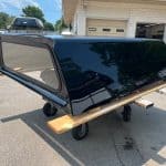 Black Chevy HD truck bed cap on a wooden stand outside.