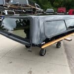 Black Chevy HD 98" truck cap with wooden side panel on wheels.