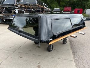 Black Chevy HD 98" truck cap with wooden side panel on wheels.