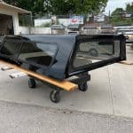 Black truck bed cap for Chevy HD 98" with tinted windows and wooden side panels.