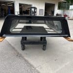 Black truck bed cap for Chevy HD 98" with tinted window and wooden side supports.
