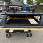 Matte black truck cap for Toyota Tacoma with roof racks and window.