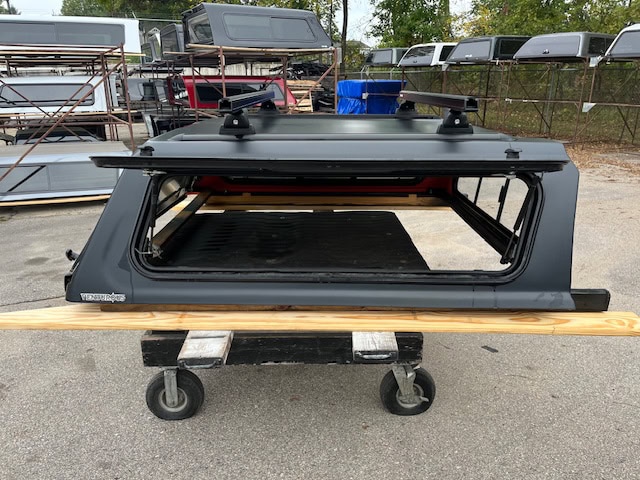 Matte black truck cap for Toyota Tacoma with roof racks and window.
