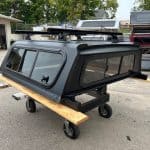 Matte black truck cap for Toyota Tacoma with roof rack and side windows.