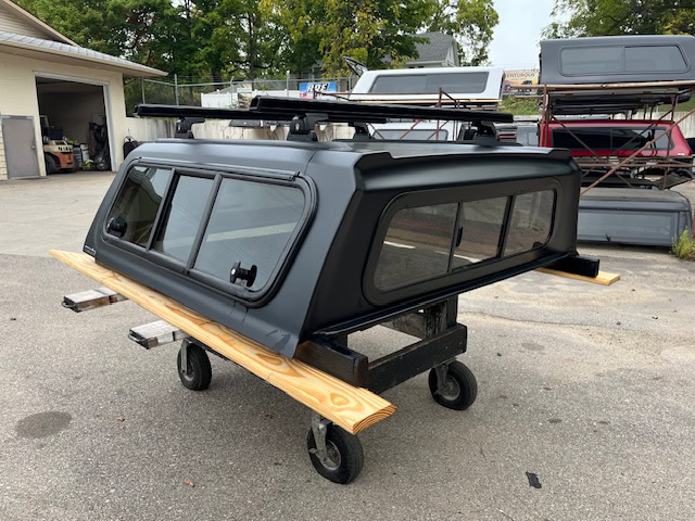 Matte black truck cap for Toyota Tacoma with roof rack and side windows.