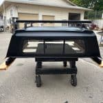 Matte black truck cap for Toyota Tacoma with roof rack and side supports.