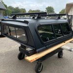 Matte black truck cap for Toyota Tacoma with roof rack and windows.