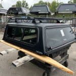Matte black truck cap for Toyota Tacoma with window panels and roof rack.