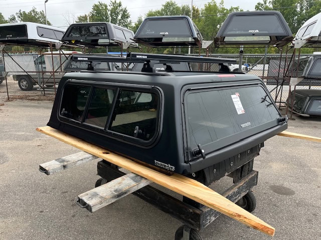 Matte black truck cap for Toyota Tacoma with window panels and roof rack.