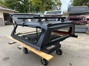Matte black truck cap for Toyota Tacoma with roof rack and side windows.