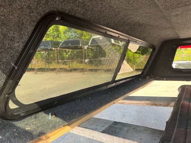 Side window of truck cap with tinted glass and black frame.