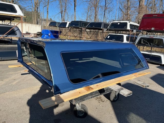 GMC HD 82.2" PNT blue truck cap with tinted windows and wooden base.