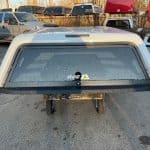 Chevy truck bed cap in Summit White with rear window and rain droplets.