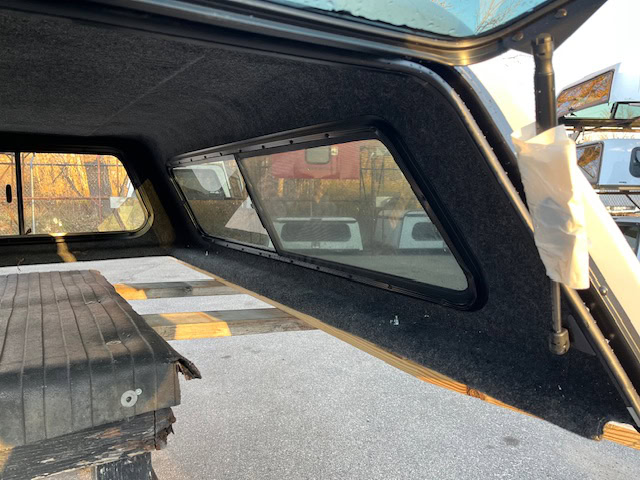 Chevy truck camper shell with black interior and side window.
