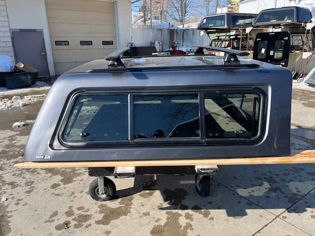 Gray truck cap with tinted windows for F150, on a dolly outside.
